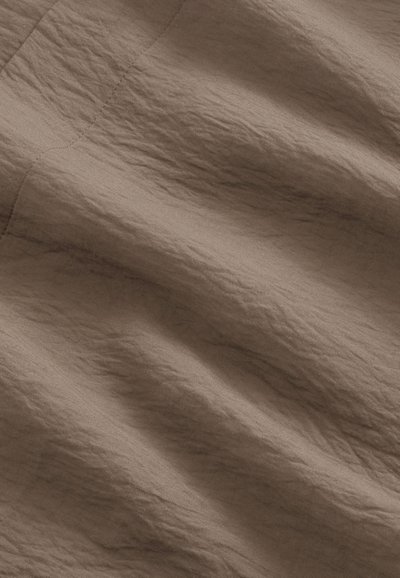 Tissu marron froissé avec une couture diagonale visible, montrant la texture et les plis doux du matériau.