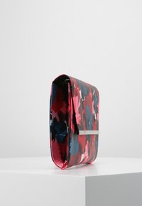 Kabelka s květinovým vzorem v růžové, červené a modré barvě. Vyrobená z lesklého materiálu, s kovovým stříbrným akcentem a skládacím designem.