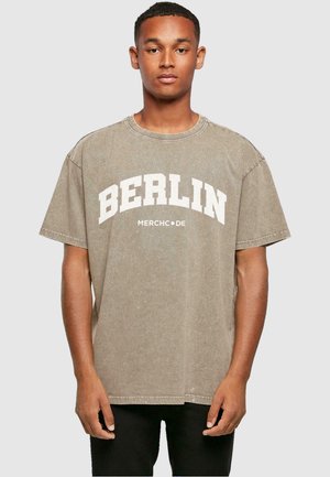 Bavlnené tričko v tlmenom khaki s krátkymi rukávmi, s výrazným textom "BERLÍN" a "MERCHCODE" nižšie v bielej farbe. Okrúhly výstrih, voľný strih.