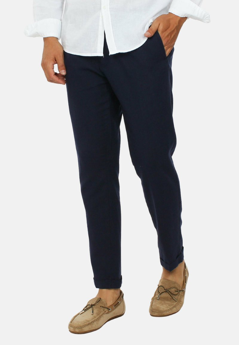 Pantaloni blu navy dal taglio sartoriale, realizzati in un tessuto morbido, con tasche inclinate e orlo a risvolto. Abbinati a mocassini color marrone chiaro.