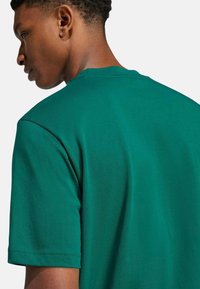T-shirt in cotone verde con collo a giro e maniche corte, caratterizzato da una texture liscia e un design semplice e monocolore.