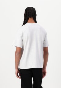 Light grey cotton t-shirt with short sleeves, a relaxed fit, and a rounded hem. No patterns or graphics. Worn with black pants.