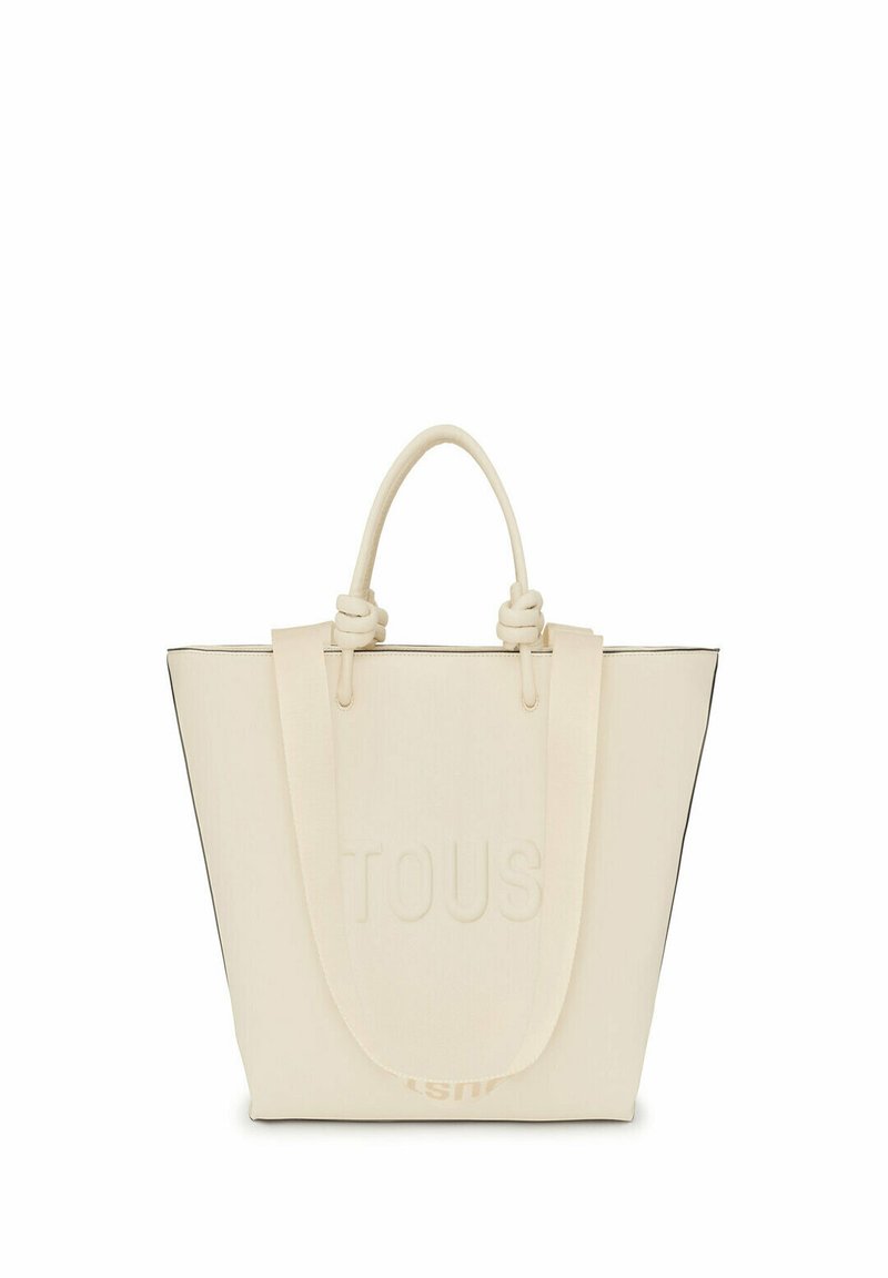 Bolso tote de color marfil con el logo "TOUS" en relieve, que cuenta con asas resistentes, un diseño estructurado y un ribete negro en contraste.