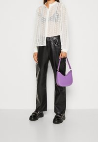 Vit spetsknäppt skjorta, svarta läderbyxor, svarta plattformsskor och en liten lila handväska med en böjd design och rem.