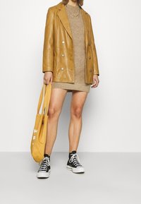 Sininen nahka kaksinkertainen bleiseri beige neulemekon päällä, yhdistetty mustiin korkeavartisiin tennareihin ja siniseen laukkuun.