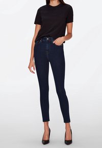Camisa negra de manga corta combinada con jeans ajustados de color azul oscuro. Los jeans tienen una cintura alta, costuras sutiles y un corte ceñido.
