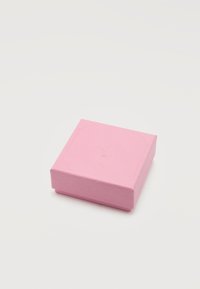 Μικρό κλειστό τετράγωνο κουτί κοσμημάτων σε ανοιχτό ροζ με διακριτικό ανάγλυφο λογότυπο στην κορυφή, τοποθετημένο σε λευκή επιφάνεια.