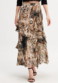 Jupe maxi fluide en marron, noir et beige avec des volants superposés, motifs floraux et abstraits, et un tissu léger et semi-transparent.