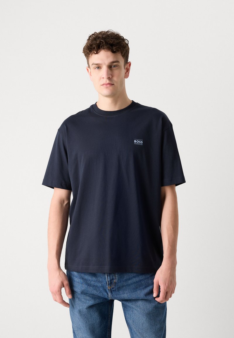 T-shirt in cotone blu navy con scollatura a girocollo e maniche corte; presenta un piccolo logo sulla parte sinistra del petto. Abbinato a jeans blu.