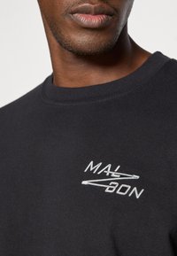 Μαύρη φούτερ μπλούζα με λαιμόκοψη, φτιαγμένη από βαμβάκι, με λευκό κεντημένο κείμενο "MALBON" και γραφικό στοιχείο. Λείο υλικό, άνετη εφαρμογή.