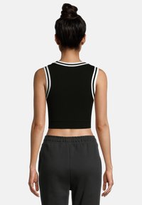 Top corto negro con rayas blancas atléticas en el escote y los agujeros de las mangas. Tela suave y diseño ajustado; combinado con pantalones de chándal grises.
