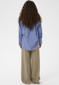 Stribet oversized skjorte i blå og hvid med lange ærmer og en buet kant, kombineret med brede beige bukser lavet af et glat stof.