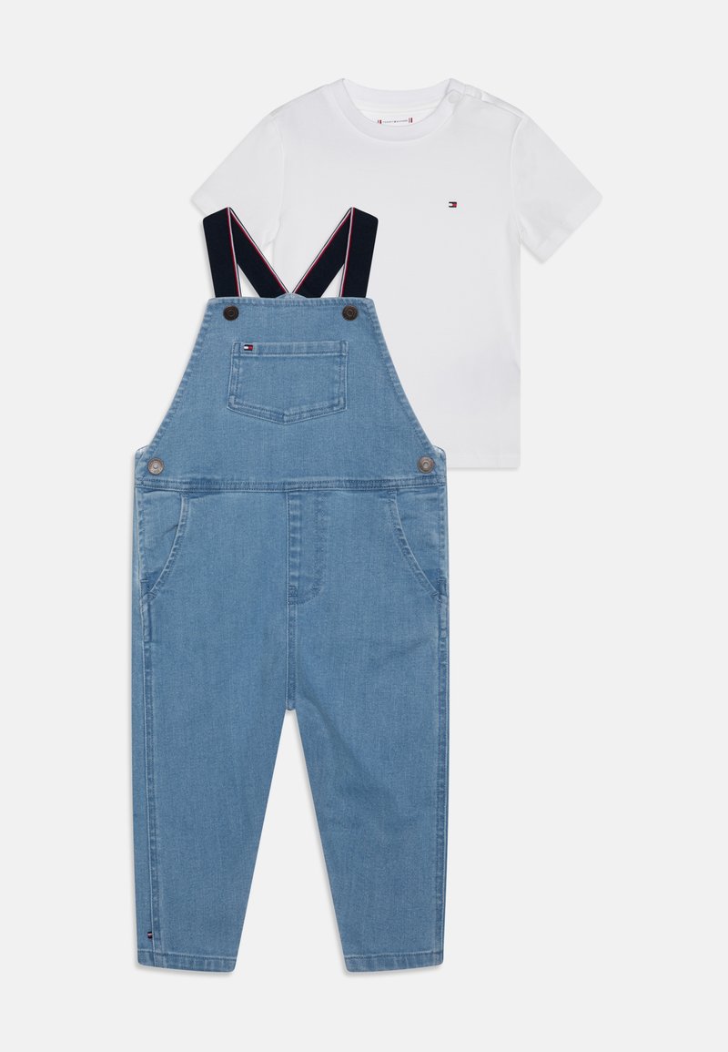 Lichtblauwe spijkeroveralls met marineblauwe bandjes, voorzien van voorzakken en een achterzak. Gekoeld met een eenvoudig wit t-shirt met korte mouwen.