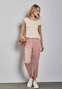 Beige přiléhavý top, růžové elegantní kalhoty a bílé tenisky. Modelka drží tkanou béžovou kabelku. Minimalistický design s hladkými texturami.