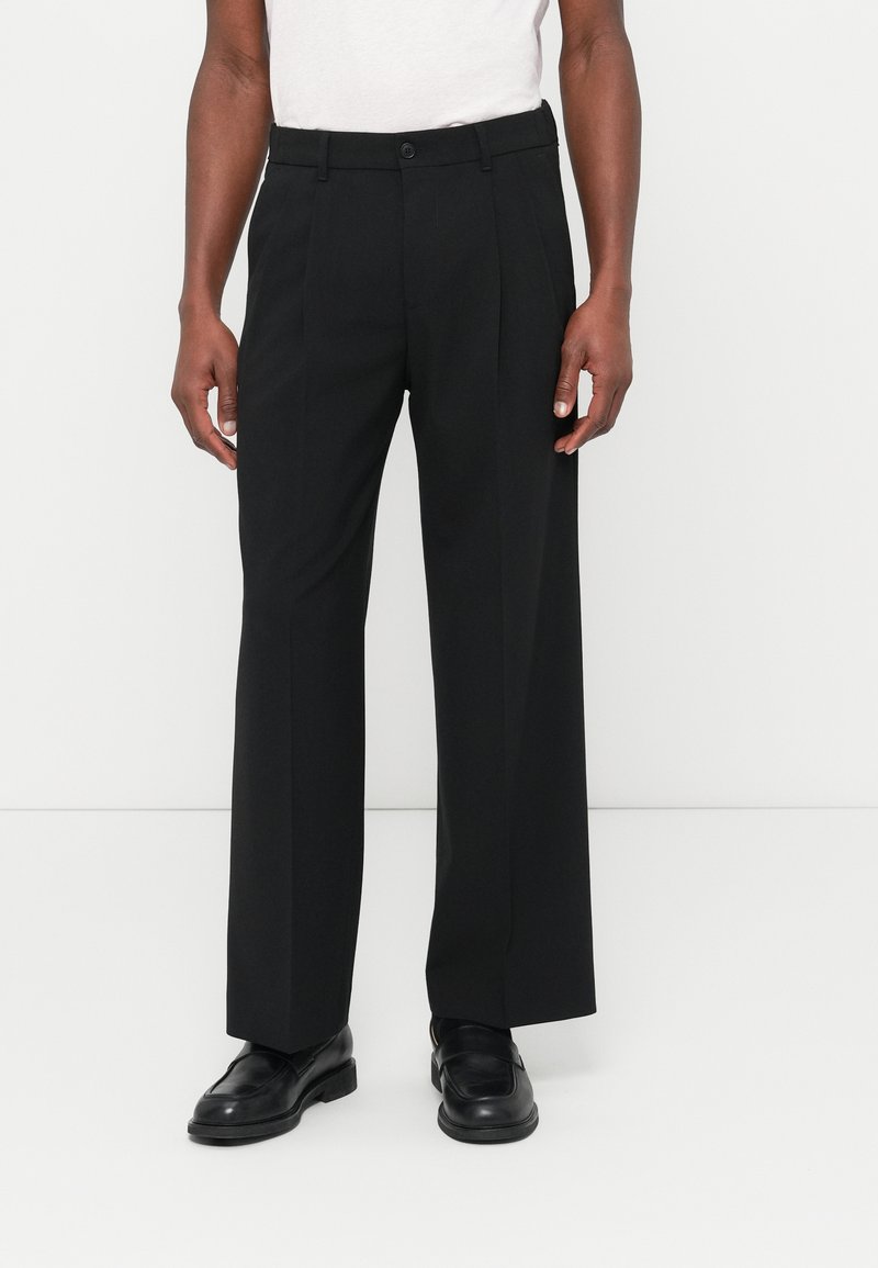 Schwarze, weit geschnittene Hose mit taillierter Passform, ausgestattet mit Knopfverschluss, glatter Textur und scharfen Biesen entlang der Vorderseite.