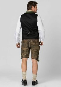Traditionelles Outfit mit einer schwarzen Weste über einem weißen Hemd und braunen Lederhosen. Die Shorts haben grüne Akzente und eine strukturierte Oberfläche.