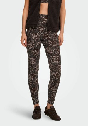 Leggings avec imprimé léopard marron et noir portés avec des baskets noires et un gilet polaire noir, montrés du milieu du torse jusqu'aux pieds.