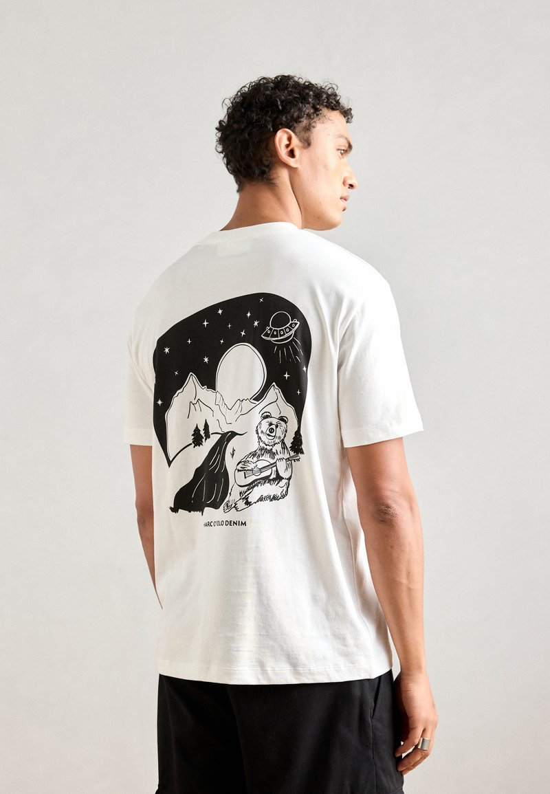Witte katoenen t-shirt met een zwarte grafische illustratie van bergen, een beer en een UFO op de achterkant. Korte mouwen, relaxte pasvorm.