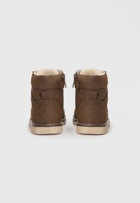 Braune Leder-Stiefeletten mit strukturierter Oberfläche, beige Innenauskleidung und zwei seitlichen Reißverschlüssen. Robuste Sohle mit kontrastierenden Nähdetails.