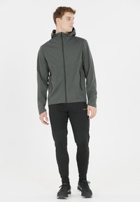 Grijze hoodie-jack met een rits aan de voorkant en twee zijzakken, gecombineerd met zwarte strakke broek met een gestructureerd ontwerp en elastische boorden.