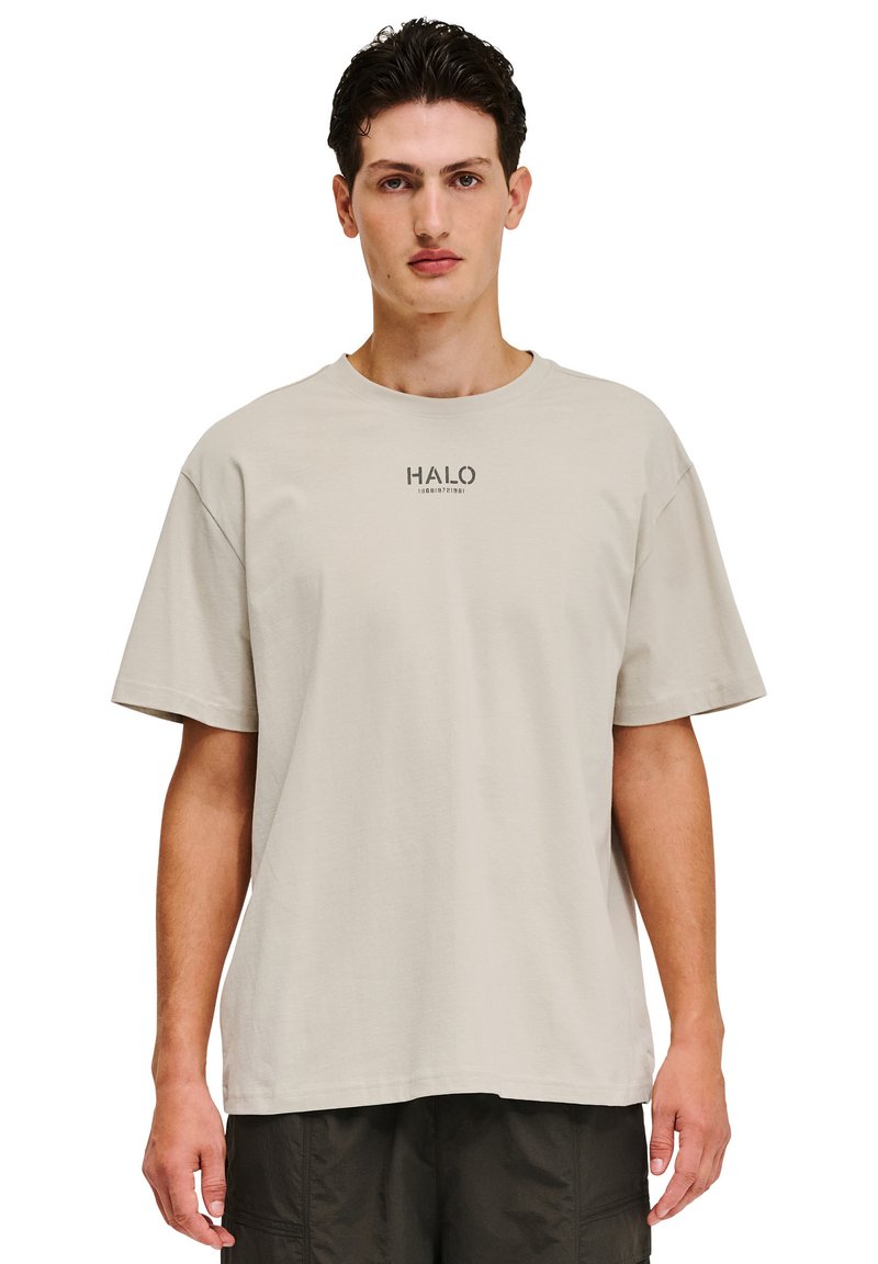 Lys beige bomulds t-shirt med en afslappet pasform. Har korte ærmer og en rund halsudskæring. Grafisk "HALO" tekst trykt i mørkt på brystet.