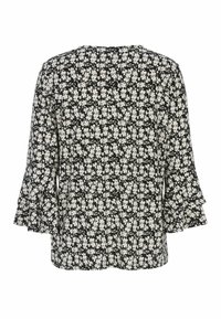 Svart blus med små vita blommor, långa ärmar med volangärmar, visad bakifrån mot en vit bakgrund.
