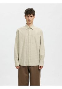 Beige rutete skjorte med knappelukking foran, spredt krage og lange ermer. Laget av lett stoff; har et subtilt rutenettmønster og avrundet kant.