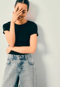 Czarna koszulka z krótkim rękawem w połączeniu z jasnoniebieskimi jeansami o wysokim stanie, prezentującymi luźny krój i subtelne przetarcia.