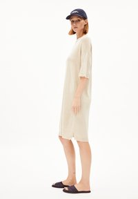 Beige knit dress with short sleeves, side slits, and ribbed hem. Worn with a dark cap and dark slide sandals. Simple, relaxed silhouette.