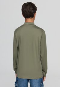 Koszulka polo z długim rękawem w kolorze oliwkowym, z płaskim kołnierzykiem i miękką fakturą, o prostym kroju, bez widocznych ozdób.