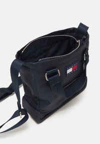 Marineblauwe nylon schoudertas met dubbele handvatten aan de bovenkant, een verstelbare schouderband, zilverkleurige hardware en een logo label met rood, wit en blauw.