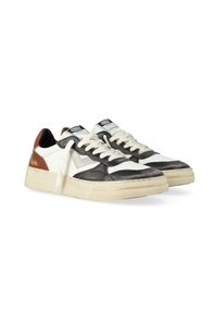 Une paire de baskets basses avec des panneaux en cuir blancs, noirs et bruns, des lacets blancs et des semelles en caoutchouc beige, placées côte à côte.