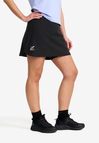 Schwarze Sportrock mit Shorts darunter, aus leichtem Material gefertigt. Hat ein Logo auf der unteren linken Seite. Wird mit Wanderschuhen getragen.