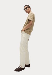 T-shirt in cotone beige, vestibilità rilassata, abbinato a jeans bianchi a gamba dritta. Completa il look con mocassini intrecciati marrone scuro e occhiali da sole neri.