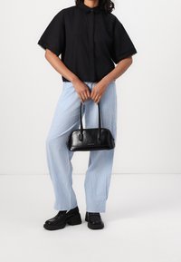 Camicetta nera a maniche corte con bordo in pizzo, abbinata a pantaloni larghi a righe blu chiaro. Borsa in pelle nera dalla forma arrotondata e con manici corti.