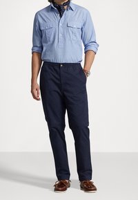 Blå chambrayskjorta med två bröstfickor, kombinerad med marinblå byxor med elastiskt midjeband och bruna mockasinliknande skor med snöre.