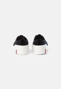 Svarta canvas sneakers med en vit gummikälla; har en texturerad överdel, vadderad krage och en liten röd logotyp på hälen.