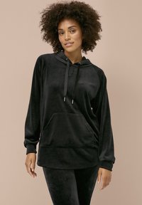Zwarte fluwelen hoodie met lange mouwen, een voorzak, een trekkoordcapuchon en een zachte textuur. Gecombineerd met bijpassende leggings.