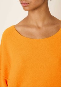 Overdimensioneret orange sweater med en rund halsudskæring, lavet af blødt, tekstureret stof. Har faldne skuldre og en afslappet pasform.
