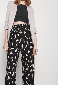 Jasnoszara marynarka nałożona na czarny prążkowany crop top, w połączeniu z czarnymi spodniami o szerokich nogawkach z białymi abstrakcyjnymi wzorami. Spodnie z elastycznym paskiem.