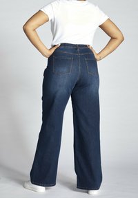 Mörkblå vida jeans med hög elastisk midja, subtila sömmar och två bakfickor, tillsammans med en enkel vit t-shirt.