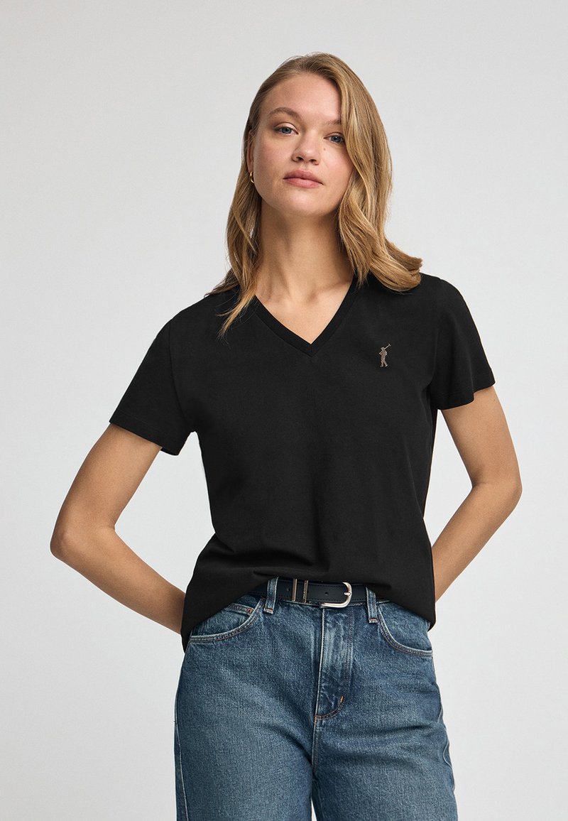 Svart bomull T-shirt med V-hals och korta ärmar, med en liten broderad detalj på vänster bröst. Kombinerad med denimjeans och ett bälte.