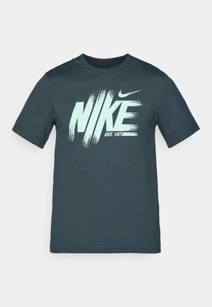 Mørk tealfarvet bomulds t-shirt med et stort hvidt og mintgrønt "NIKE" logo med penselstrøgsaccenter og teksten "EST. 1977" nedenunder.