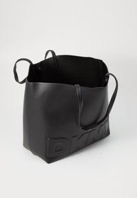 Black leather tote bag with a smooth texture, open top, two short handles, and embossed "DKNY" logo on one side.
