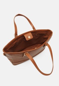Bolso tote de cuero marrón con dos asas, parte superior abierta y cierre a presión. El interior está forrado con tela marrón e incluye un bolsillo con cremallera.
