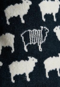Schwarzer gestrickter Stoff mit einem Muster aus weißen Schafen, wobei ein Schaf in der Mitte gestreifte Wolle hat, die einem Barcode ähnelt.