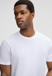 Witte katoenen t-shirt met korte mouwen en een ronde halslijn, met een gladde textuur en een minimalistisch ontwerp, gepresenteerd op een neutrale achtergrond.