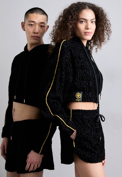 Set format din hanorac scurt negru și pantaloni scurți, țesătură texturată cu logo-ul Versace călit, accente aurii și talie elastică cu șnur.