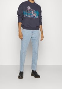 Granatowy sweter z grafiką gór i wilka, zestawiony z jasnoniebieskimi dżinsami i czarnymi botkami Chelsea. Posiada prążkowane mankiety i dół.