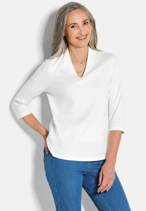Witte V-hals top met driekwartmouwen, gemaakt van een gladde stof; casual gedragen met een blauwe spijkerbroek.